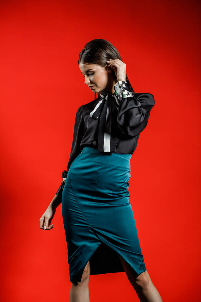 Stúdió portré fiatal modell alkalmi ruha, piros háttér. Fiatal nő fekete inget és kék szoknya pózol stúdió  - Fotó, kép