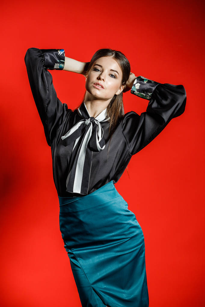 Estudio retrato de modelo joven en ropa casual sobre fondo rojo. Mujer joven en camisa negra y falda azul posando en el estudio
  - Foto, imagen