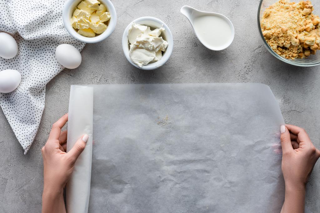 Colpo ritagliato di donna in possesso di carta da forno con ingredienti disposti per torta su tavolo grigio
 - Foto, immagini