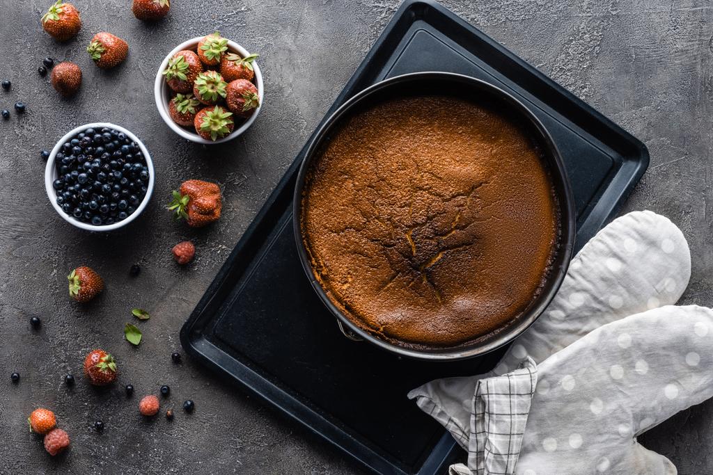 flache Liege mit selbst gebackenem Kuchen, frischen Beeren und Backtuch auf dunkelgrauer Tischplatte - Foto, Bild
