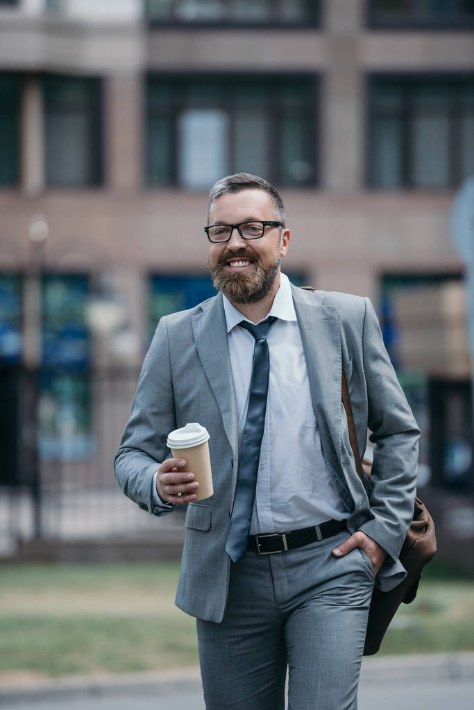 красивый улыбающийся бизнесмен ходит по улице и держит кофе в бумажной чашке
 - Фото, изображение