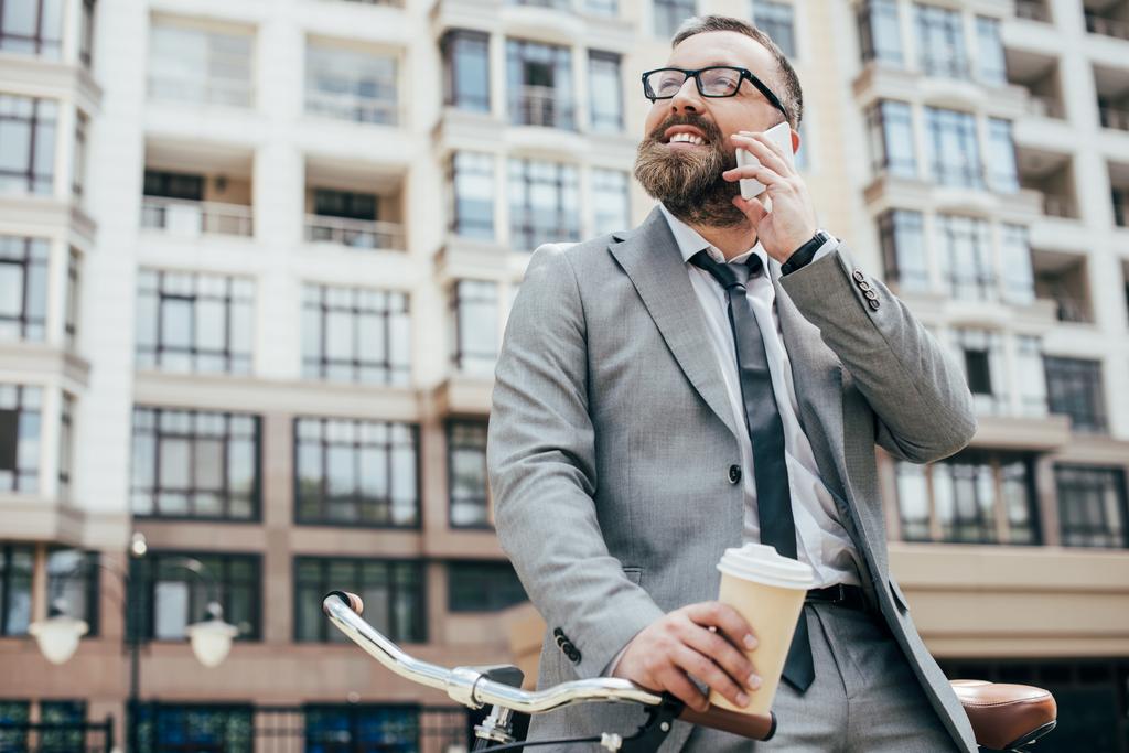 bärtiger Geschäftsmann mit Fahrrad, Einwegbecher Kaffee in der Hand und Smartphone im Gespräch - Foto, Bild