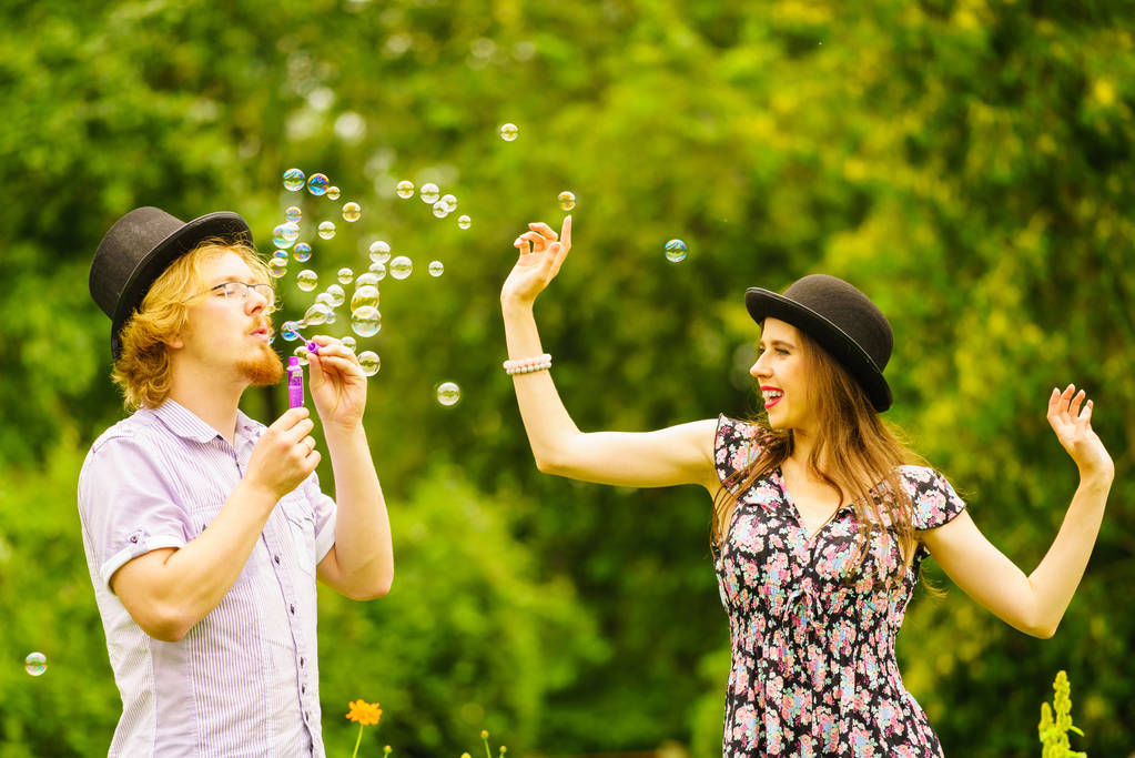 Heureux couple hipster drôle de jouer ensemble souffler des bulles de savon en plein air dans le parc de printemps. - Photo, image