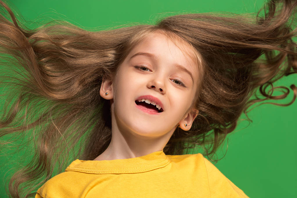 De gelukkige tiener meisje permanent en glimlachend tegen groene achtergrond. - Foto, afbeelding