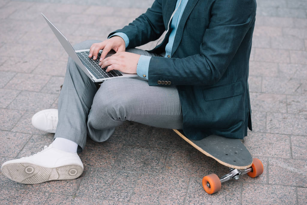 bijgesneden beeld van de mens met behulp van laptop en zittend op het skateboard - Foto, afbeelding