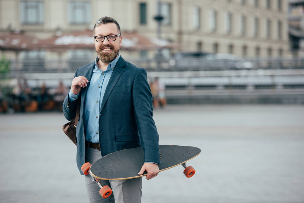 стильний бородатий чоловік зі шкіряною сумкою та скейтбордом у місті
 - Фото, зображення