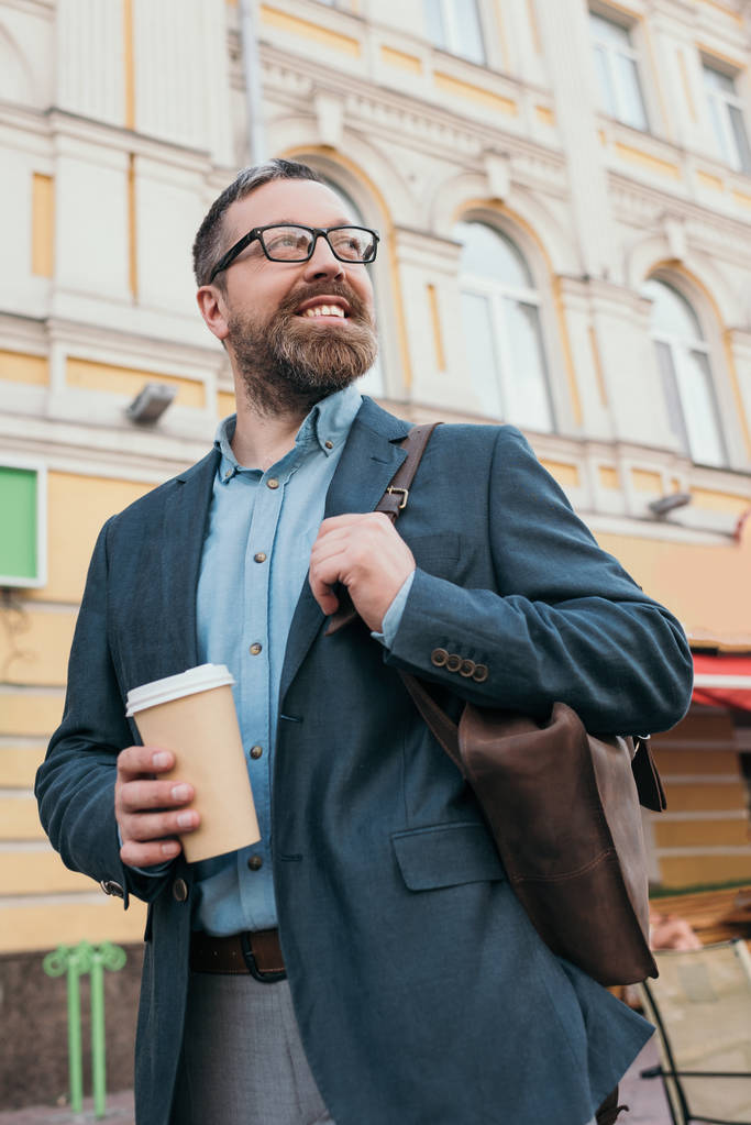 stijlvolle Glimlachende man met lederen tas en wegwerp kopje koffie in de stad - Foto, afbeelding