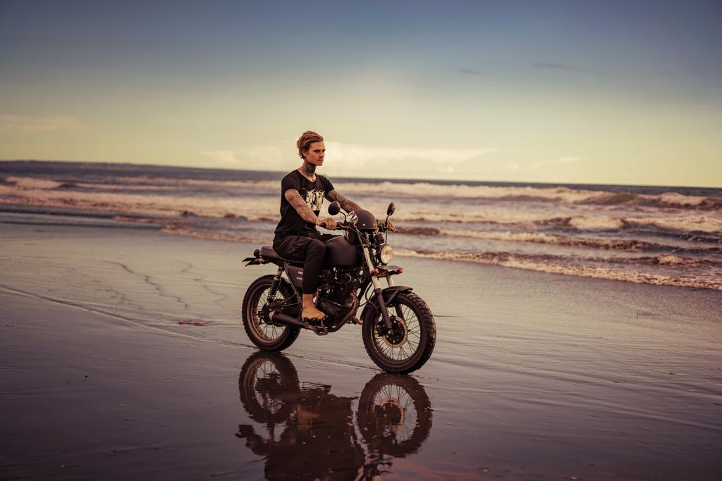 guapo ciclista tatuado montar en moto en la playa del océano durante las vacaciones
 - Foto, Imagen