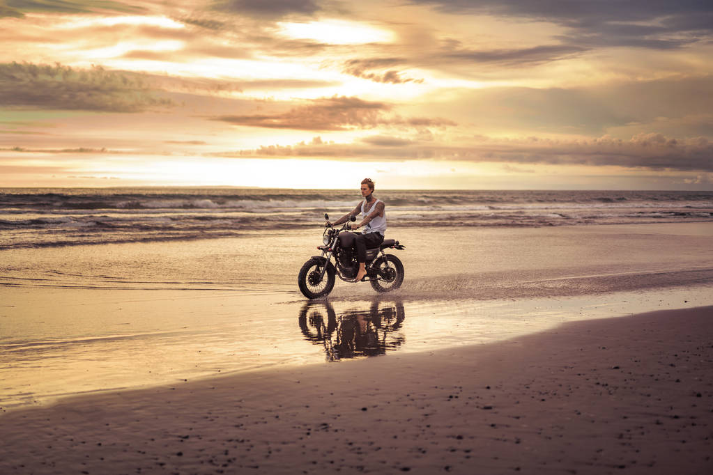 татуированный байкер на мотоцикле по океанскому пляжу во время заката
 - Фото, изображение
