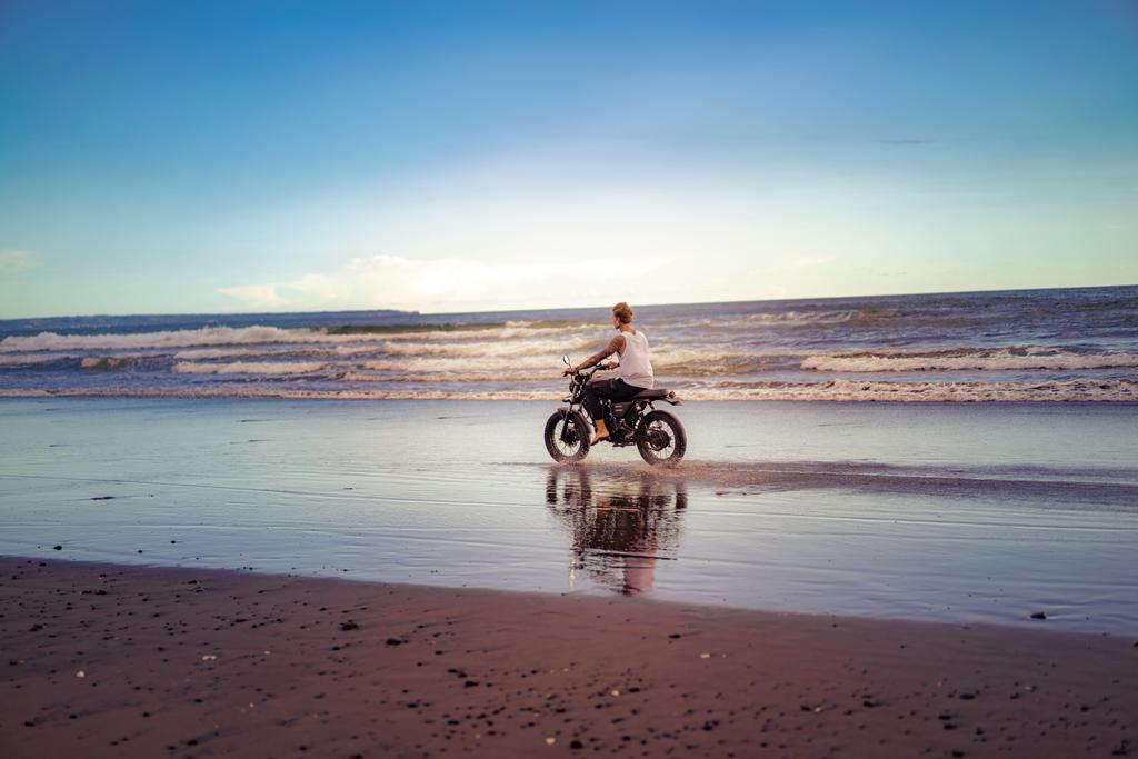 Tätowierter Mann fährt Motorrad am Strand des Ozeans bei Sonnenaufgang - Foto, Bild