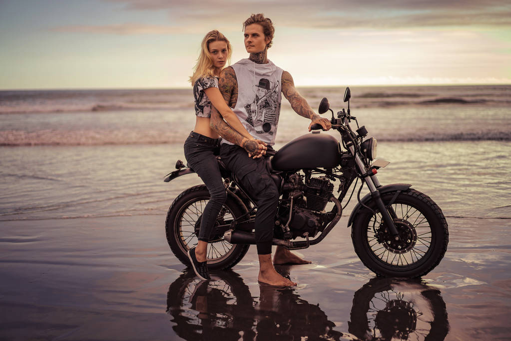 couple tenant la main et assis sur la moto sur la plage de l'océan
  - Photo, image