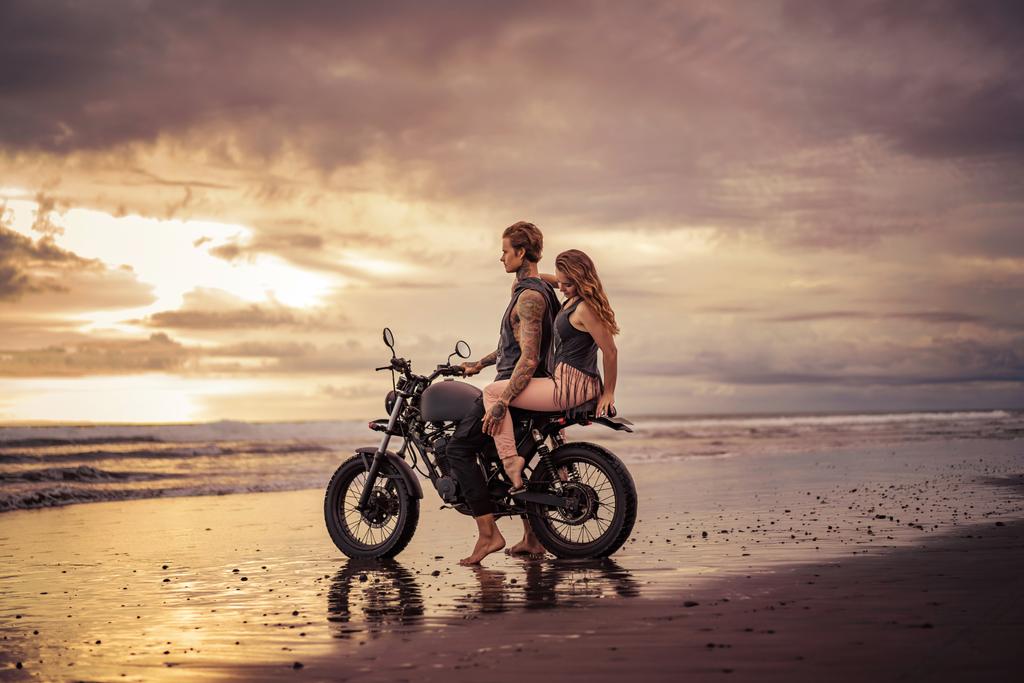 novio y novia abrazándose en motocicleta en la playa durante el amanecer
  - Foto, Imagen