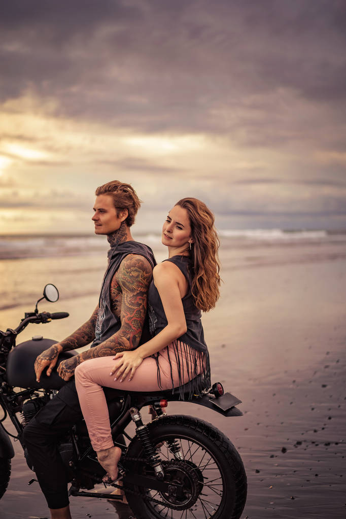 Παθιασμένος φίλη και φίλο της κάθεται σε μοτοσικλέτα στην παραλία κατά την Ανατολή του ηλίου  - Φωτογραφία, εικόνα
