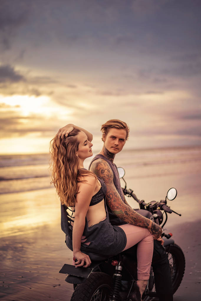 fidanzato sensuale e fidanzata seduta sulla moto in riva al mare durante la bella alba
  - Foto, immagini
