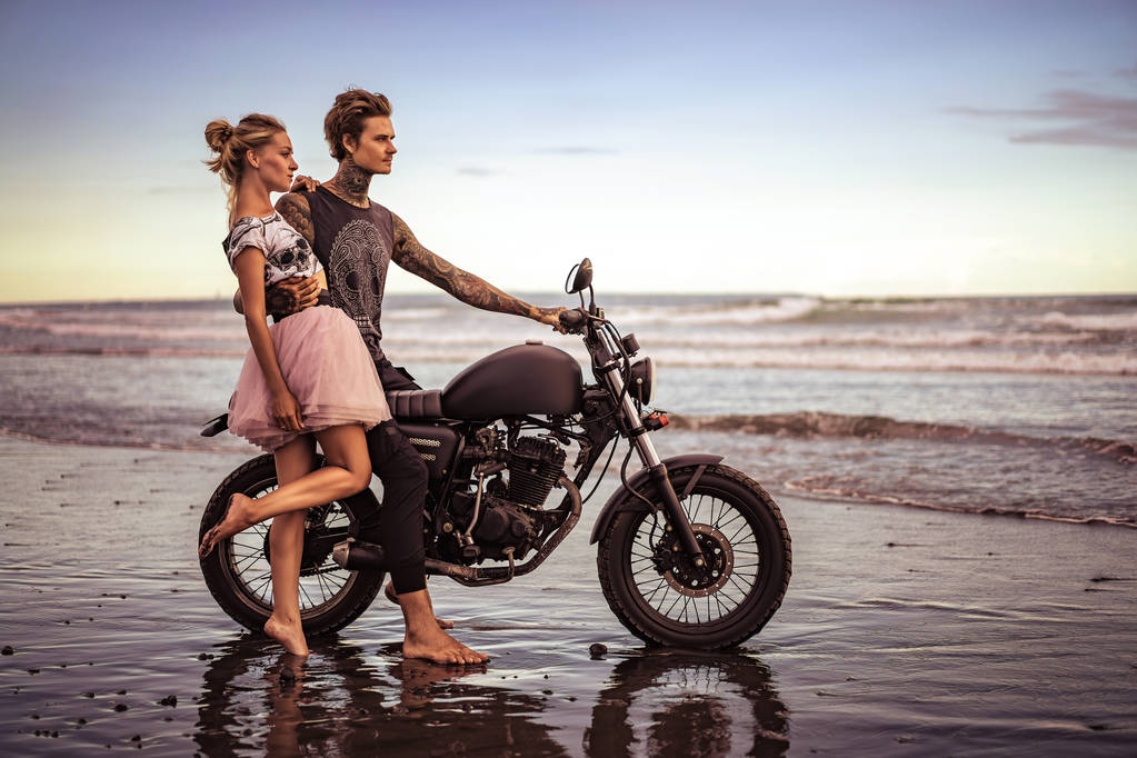 хлопець обіймає дівчину і сидить на мотоциклі на океанічному пляжі
 - Фото, зображення