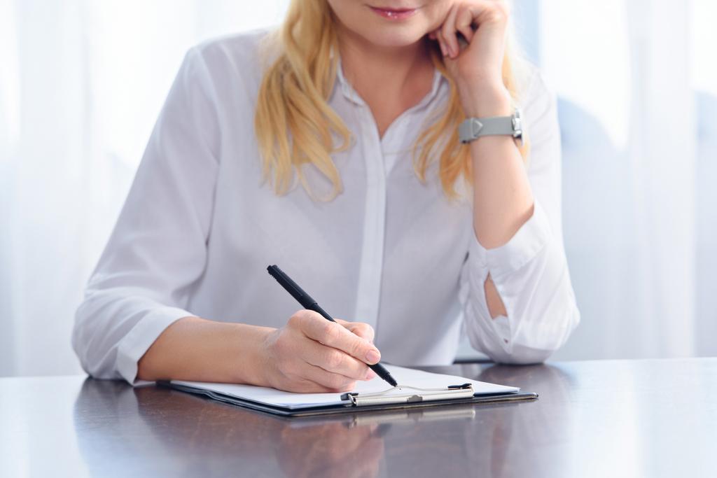 обрізане зображення жінки-радника, що пише в буфері за столом в офісі
  - Фото, зображення