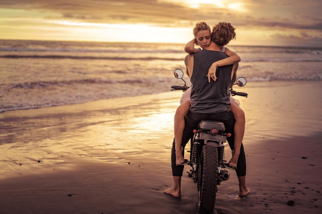 heteroseksueel paar knuffelen op motorfiets op oceaan strand tijdens de prachtige zonsopgang  - Foto, afbeelding