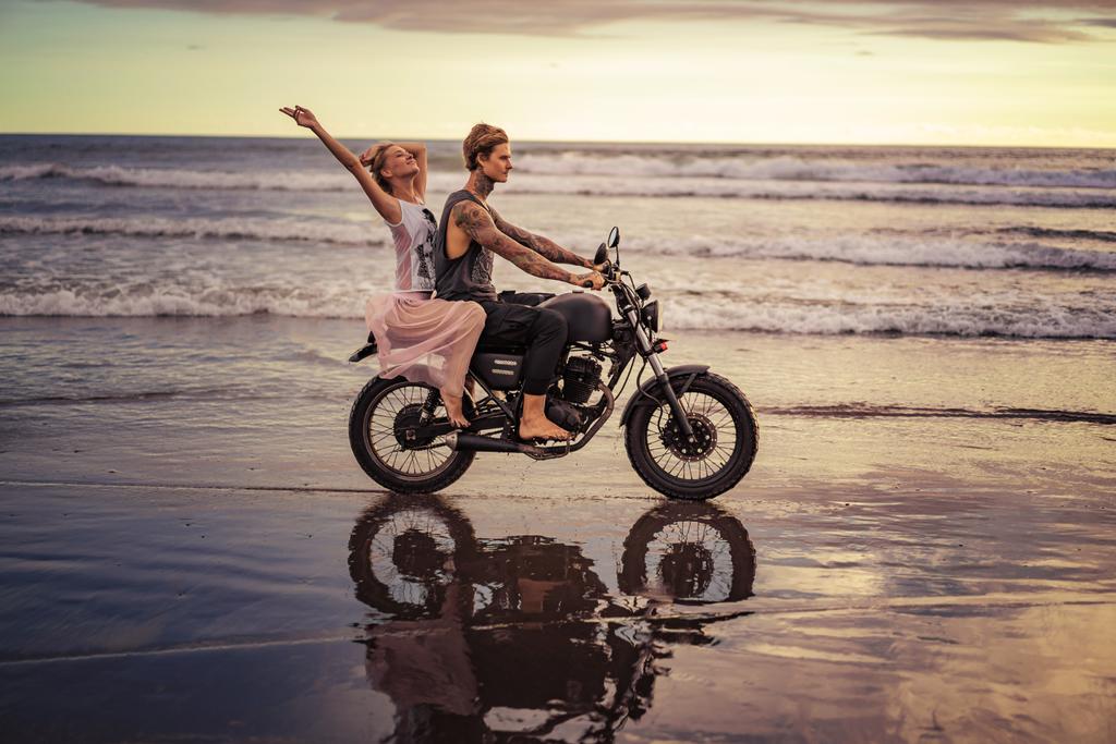 χαρούμενος ο φίλος και φίλη ιππασία μοτοσικλέτα στον ωκεανό στην παραλία κατά την Ανατολή του ηλίου - Φωτογραφία, εικόνα