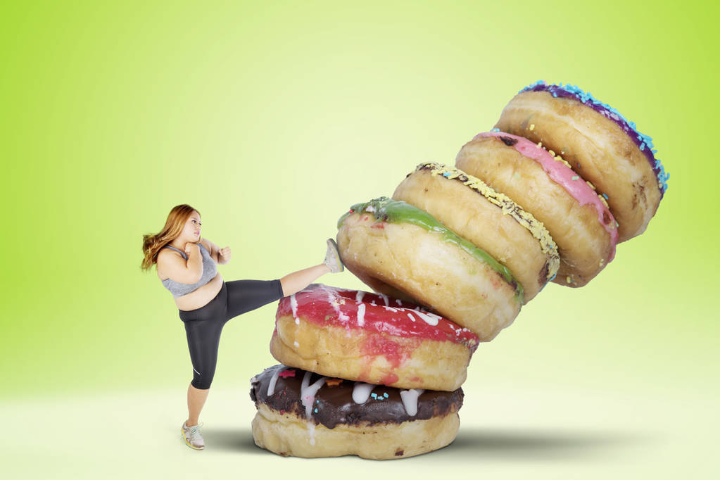 Obraz kobiety tłuszczu odmawiają jedzenia słodkich pokarmów przez kopanie kupie pączki. Strzał z tło zielony ekran - Zdjęcie, obraz