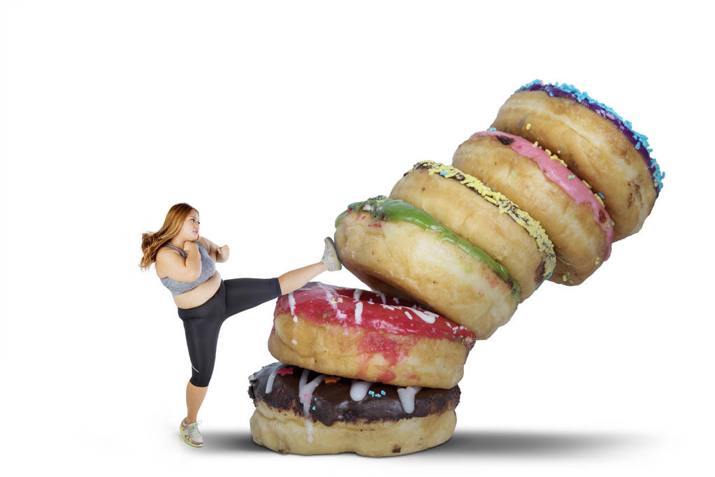 Concepto de dieta. Mujer con sobrepeso que se niega a comer alimentos dulces pateando donas, aislado sobre fondo blanco
 - Foto, Imagen