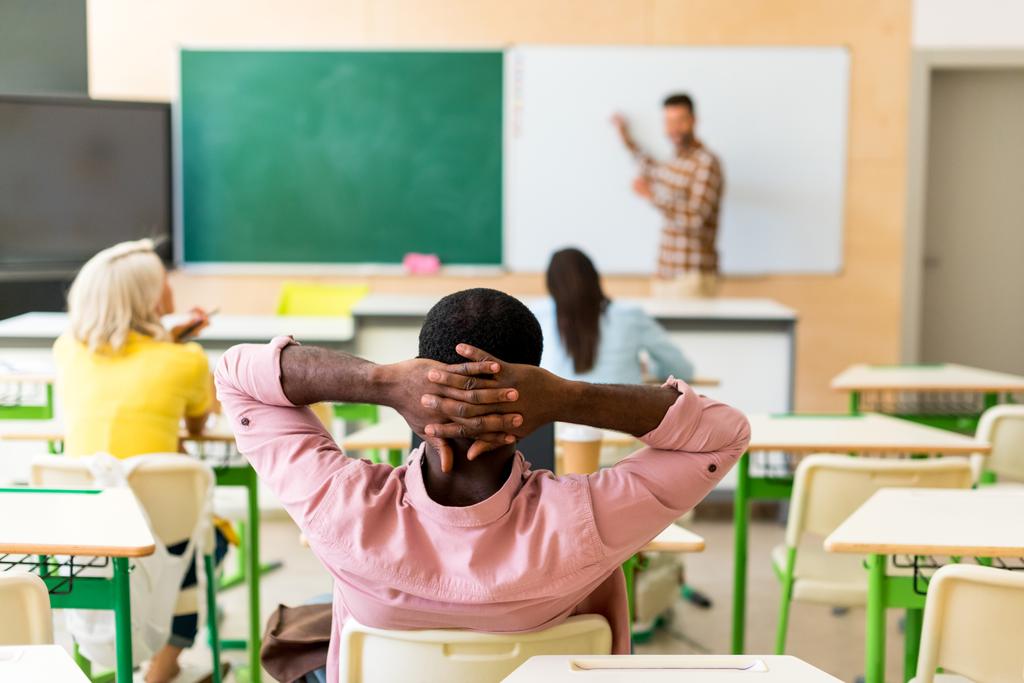 Widok z zrelaksowany Afryki amerykański student siedzi w klasie podczas lekcji z tyłu - Zdjęcie, obraz