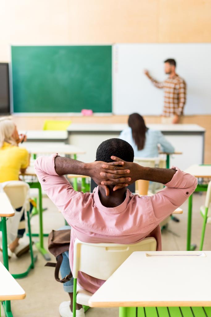 Achteraanzicht van ontspannen Afrikaanse Amerikaanse student tijdens de les aan klas zitten - Foto, afbeelding