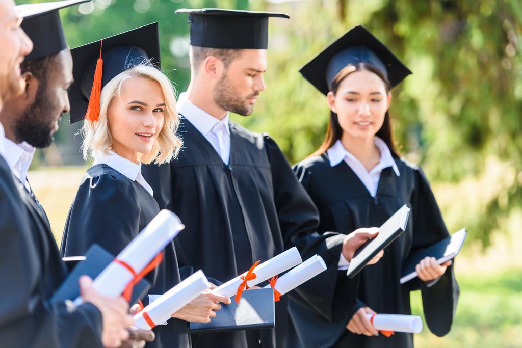 studenti laureati con successo in mantelli e cappelli in possesso di diplomi arrotolati
 - Foto, immagini