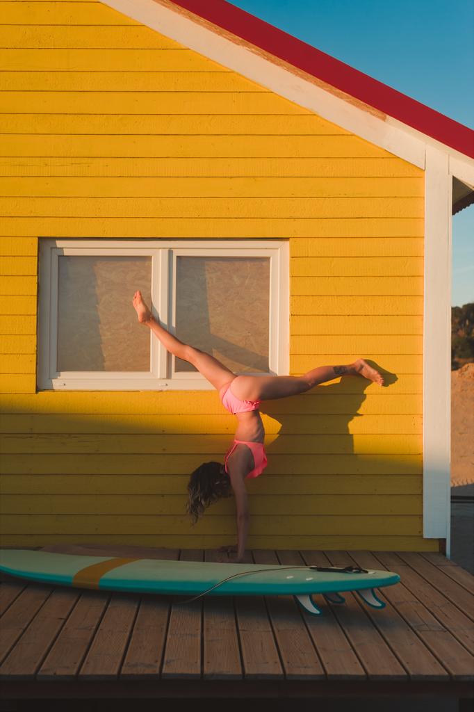 jonge vrouw met een roze bikini reputatie op handen tegen geel gebouw met surfen bord in de buurt van door in Portugal - Foto, afbeelding