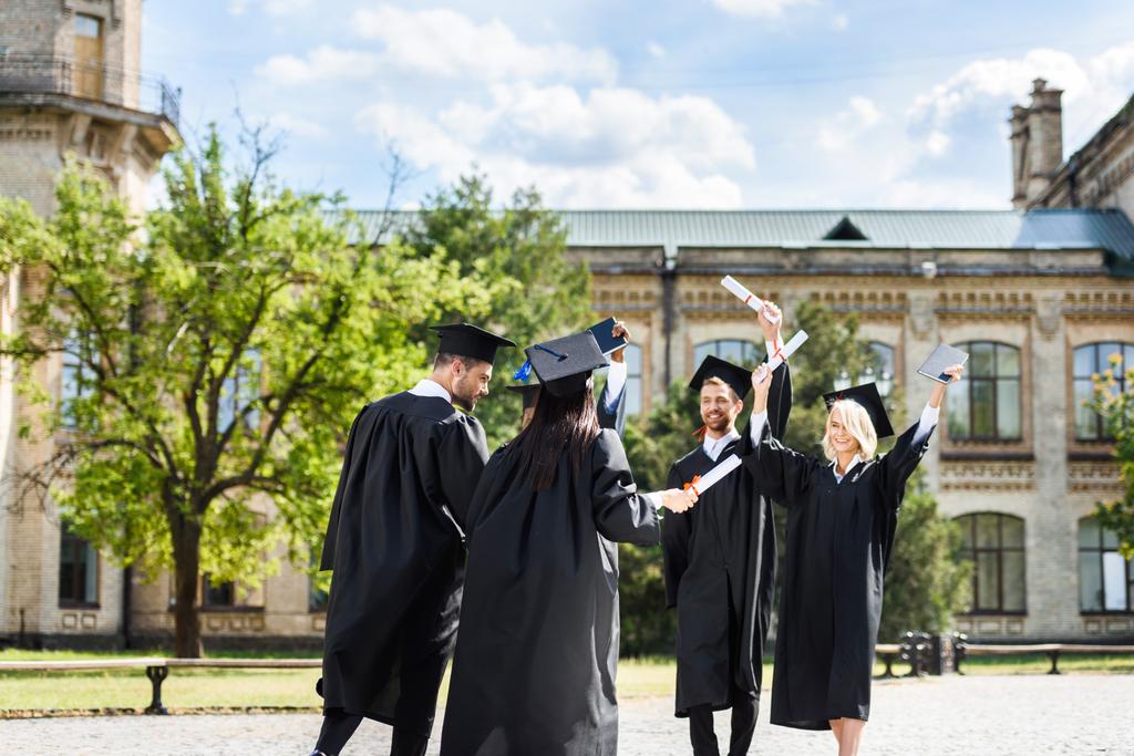 молоді випускники з дипломами вітають один одного в саду коледжу
 - Фото, зображення
