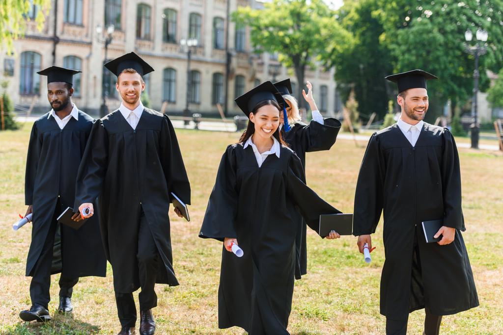 молодих випускників у накидах, що ходять університетським садом
 - Фото, зображення