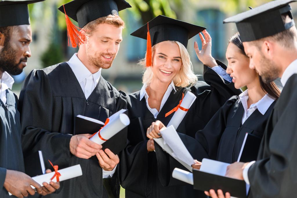 Lächelnde multiethnische Hochschulabsolventen in Umhängen mit Diplomen - Foto, Bild