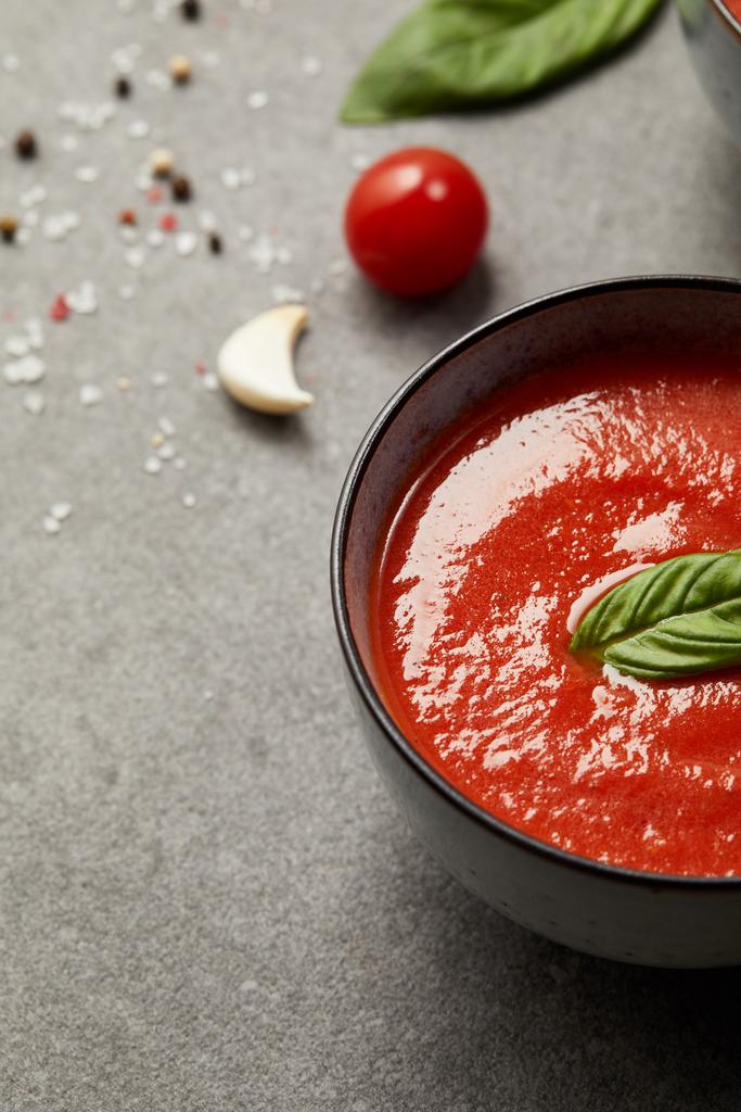 томатный суп с базиликом в тарелках и помидорами с чесноком на сером столе
 - Фото, изображение
