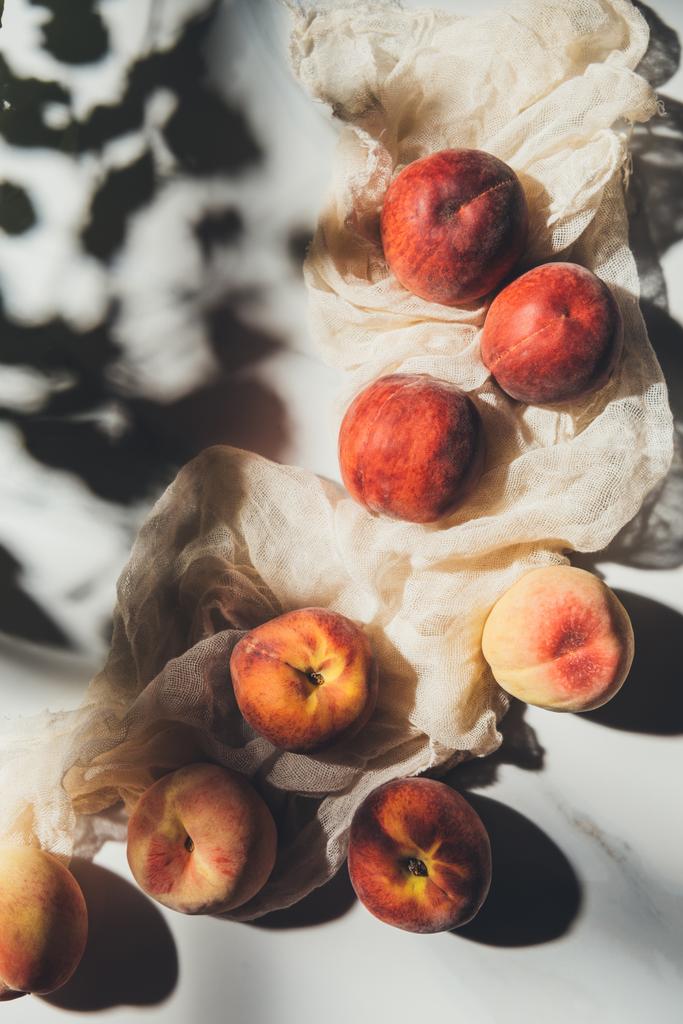Плоский лежал с спелыми персиками и марлей на светлом мраморном столе с тенями
 - Фото, изображение