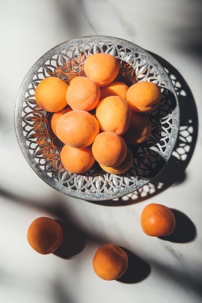 flat lay with ripe apricots in metal bowl on light marble surface with shadows - Photo, Image