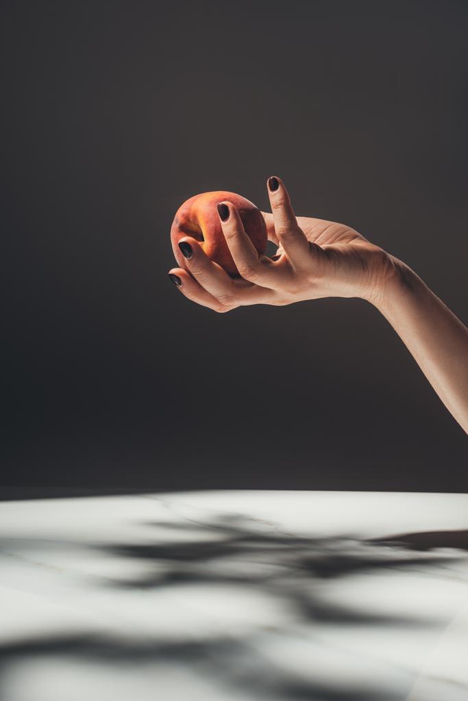 partial view of woman holding ripe peach in hand on black background - Photo, Image