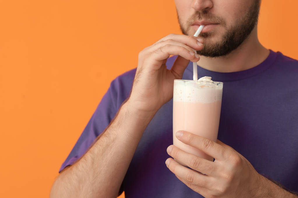 Mladý muž se sklem lahodný mléčný koktejl na barvu pozadí - Fotografie, Obrázek
