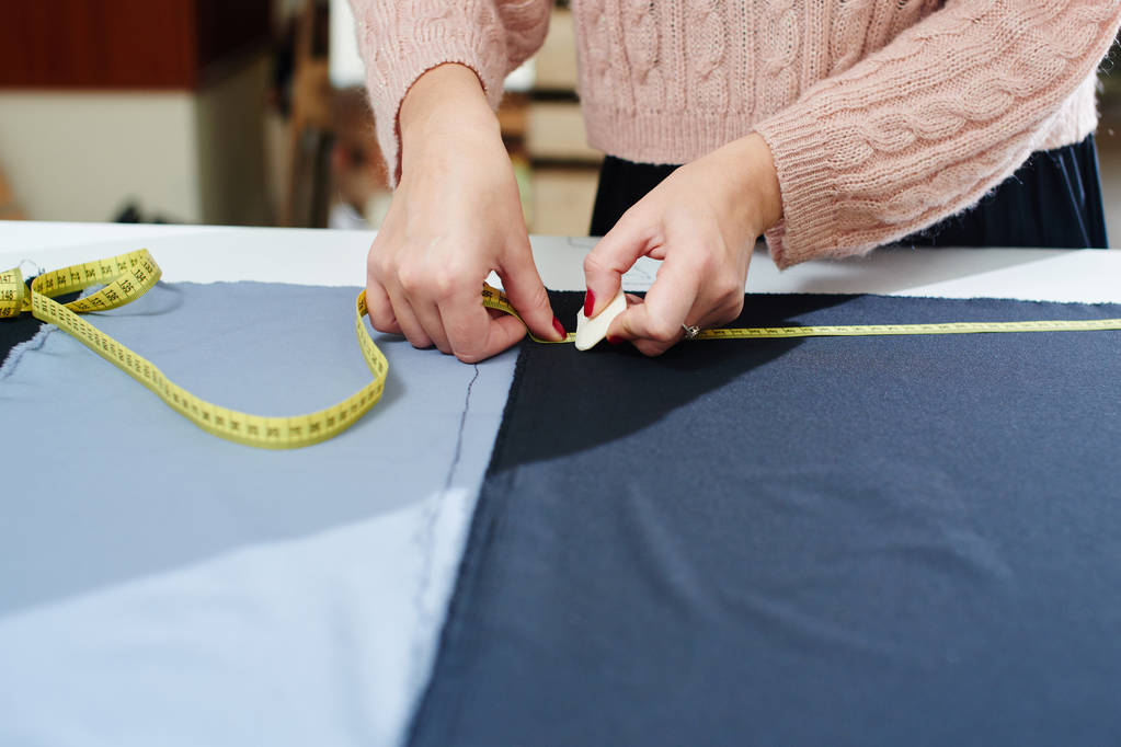 sastre usando cinta métrica mientras dibuja con tiza en textil en atelier, creación de ropa en atelier
 - Foto, imagen