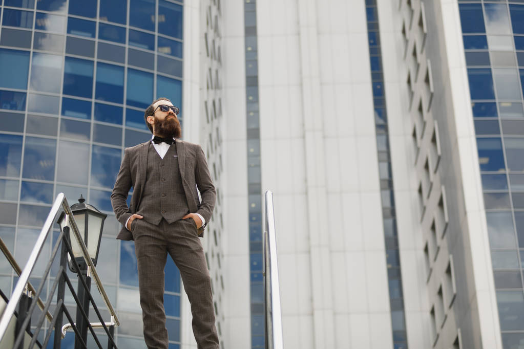 Сучасний бізнесмен. Впевнений молодий чоловік в повному костюмі, дивлячись далеко, стоячи на відкритому повітрі з міським пейзажем на задньому плані
 - Фото, зображення