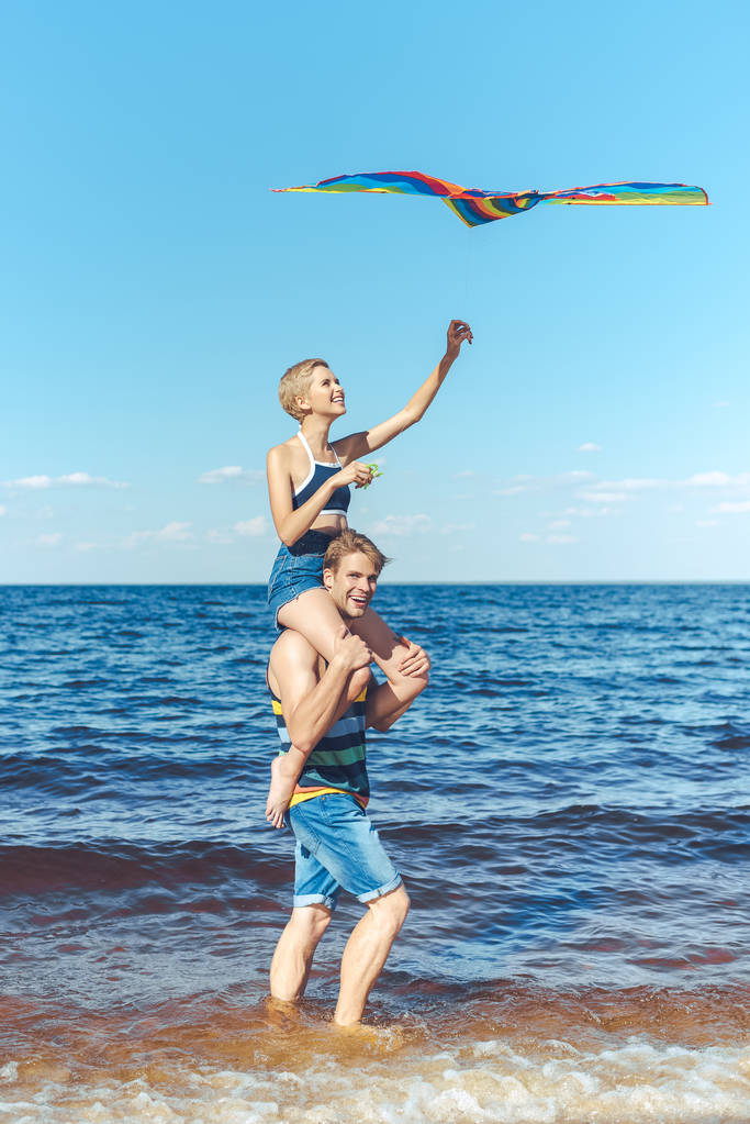 молодая женщина с цветным воздушным змеем сидит на плечах своих парней на пляже
 - Фото, изображение