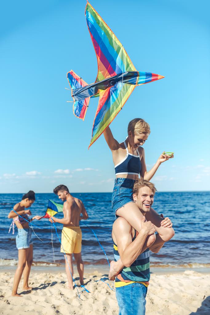 selective focus of interracial group of friends with kites having fun on sandy beach - Photo, Image