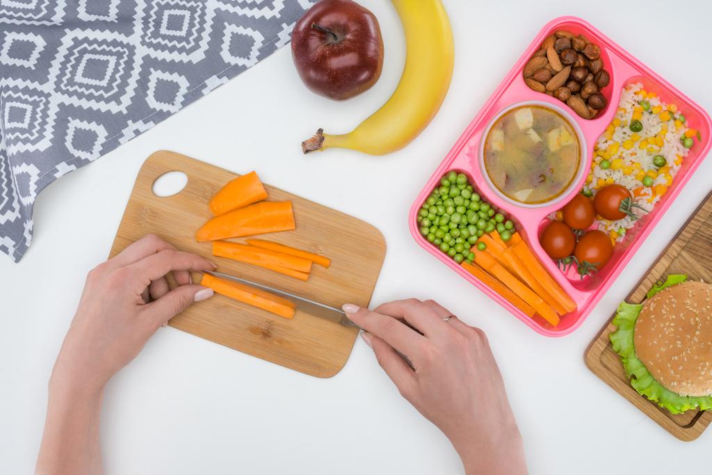bijgesneden afbeelding van moeder voorbereiden kids diner voor school en snijden wortel - Foto, afbeelding