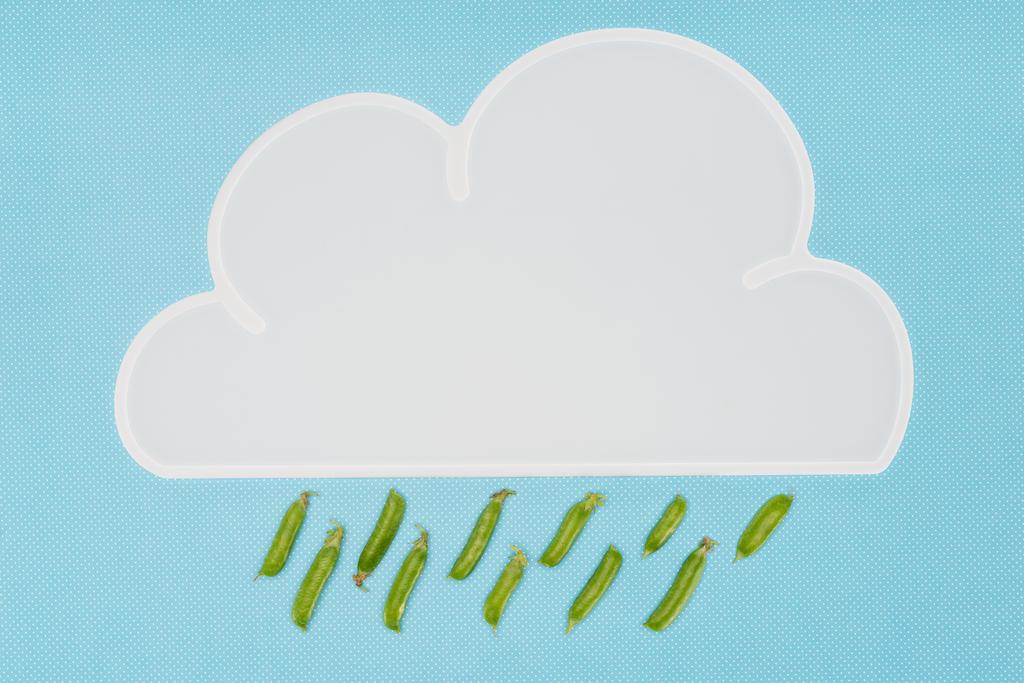 top view of white napkin in shape of cloud with rain of pea pods isolated on blue - Photo, Image
