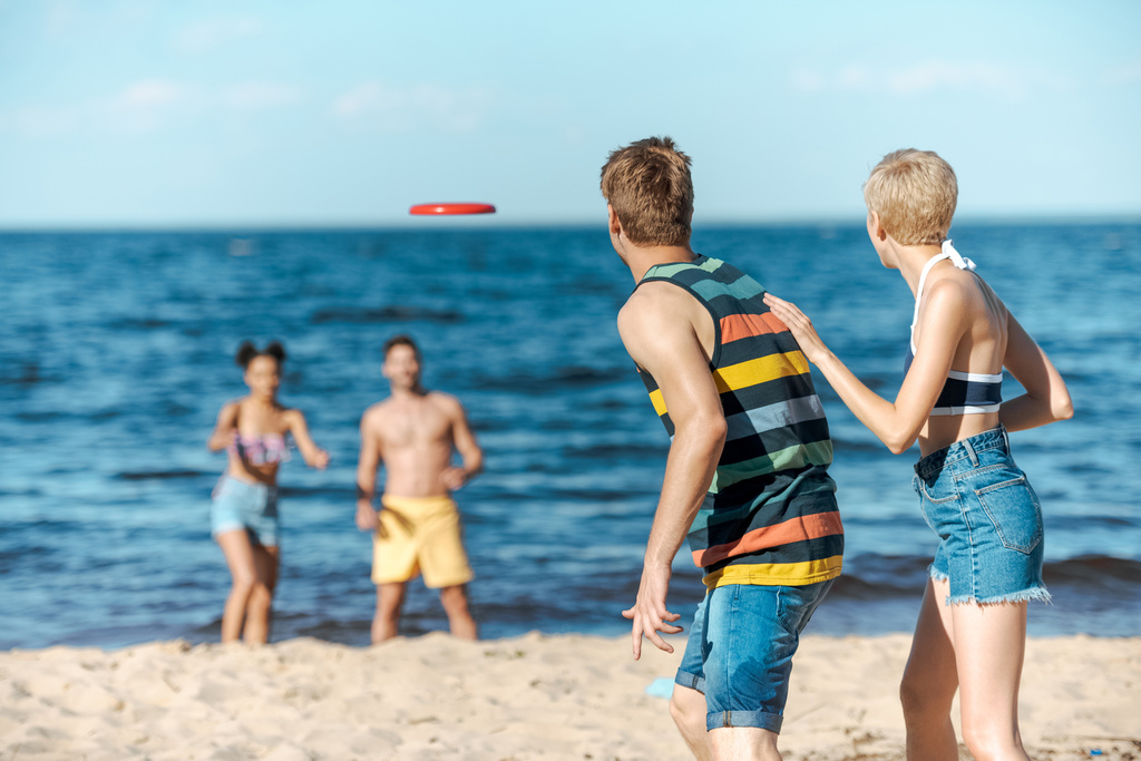 Selektivní fokus mnohonárodnostní přátel hrát s letící disk společně na pláži - Fotografie, Obrázek