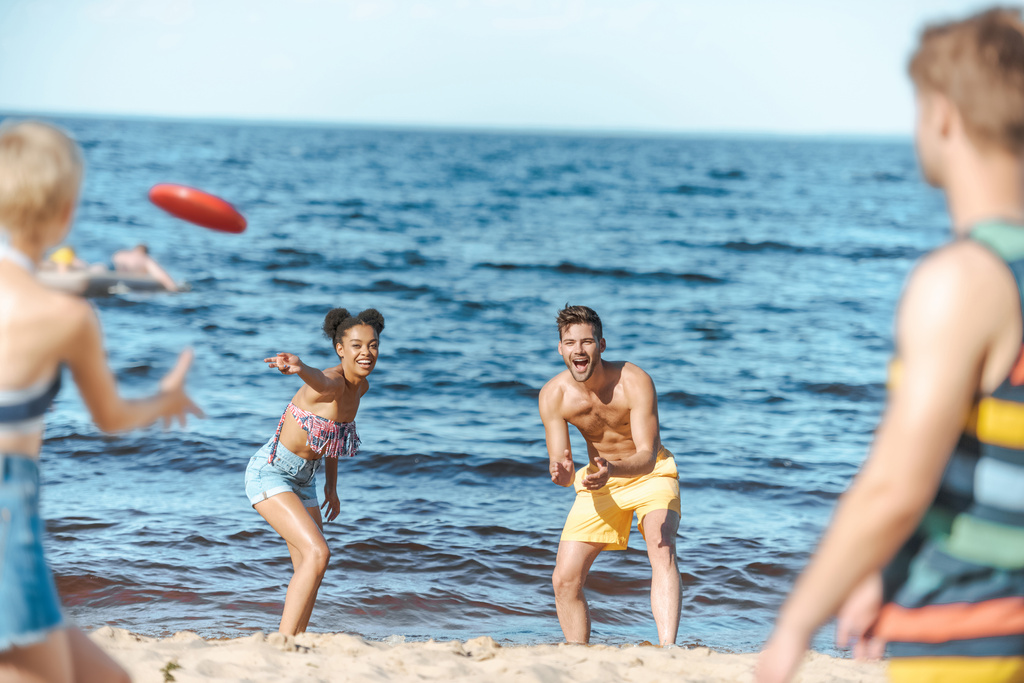 messa a fuoco selettiva di amici multirazziali che giocano con disco volante insieme sulla spiaggia
 - Foto, immagini