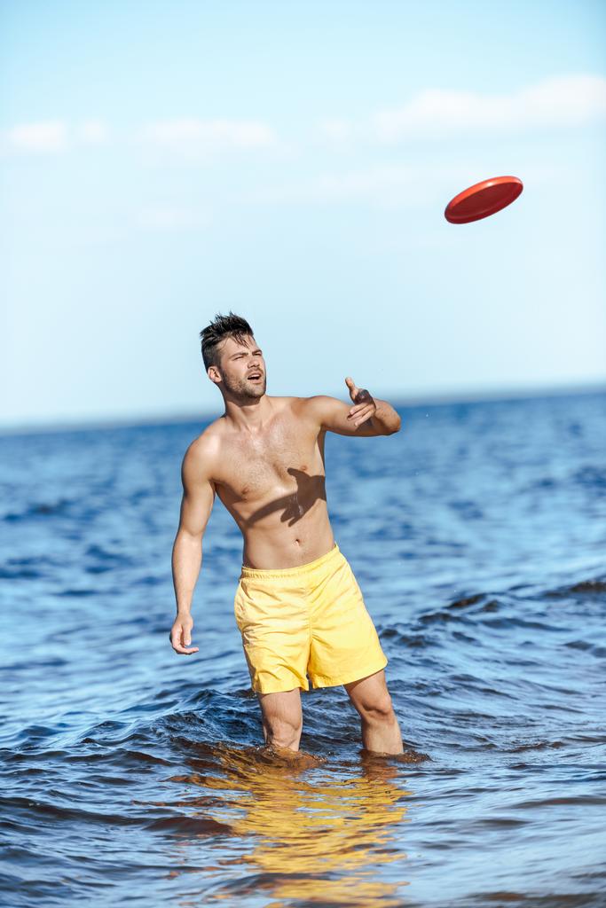 young man throwing flying disc while standing in sea on summer day - Photo, Image