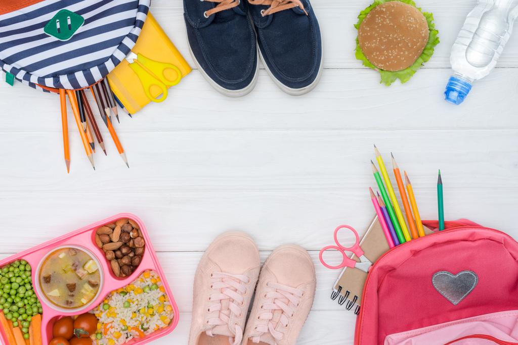 vista dall'alto del vassoio con pranzo per bambini, borse scolastiche e scarpe sul tavolo bianco
 - Foto, immagini