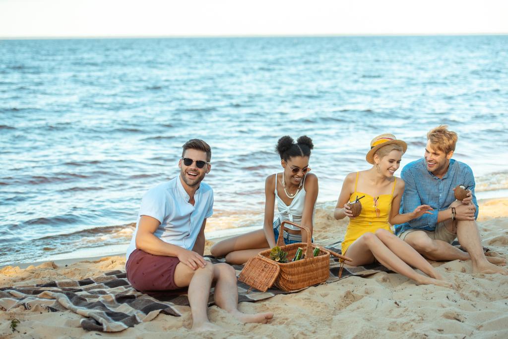 Interracial, mosolygó fiatal meg itallal pihenő homokos strandon együtt a nyári nap - Fotó, kép