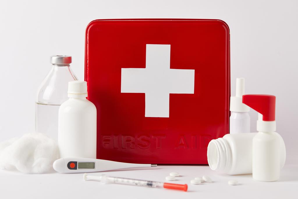 κοντά shot της κόκκινο πρώτες βοήθειες kit box με διαφορετικές ιατρικές φιάλες και προμήθειες σε λευκό - Φωτογραφία, εικόνα