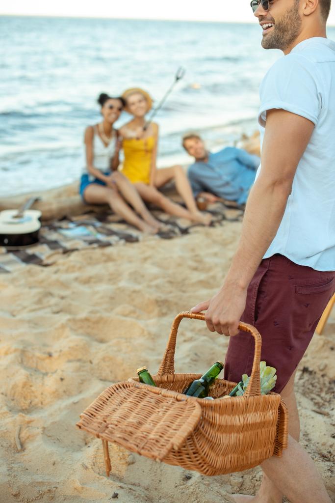 vista parziale dell'uomo con cesto da picnic e amici multietnici sulla spiaggia di sabbia
 - Foto, immagini