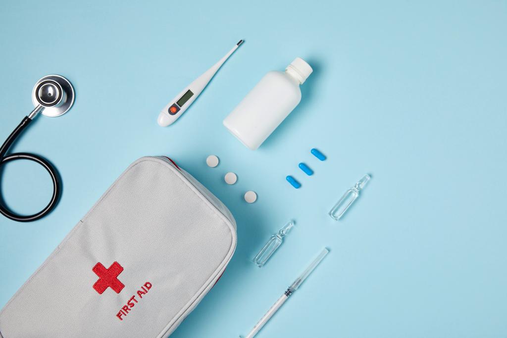 top view of white first aid kit bag with stethoscope and various medicines on blue surface - Photo, Image